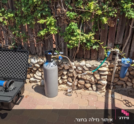 מיכל גז, צינור ומד לחץ ליד גדר עץ